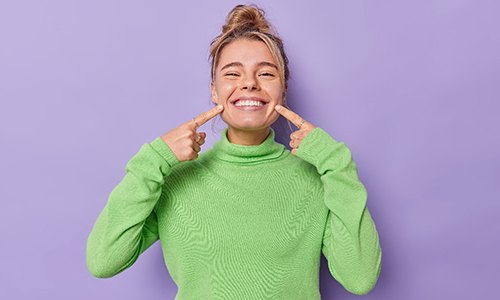 Woman in green sweater pointing at her smile