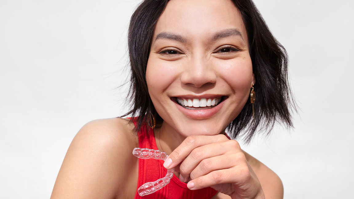 Young woman smiling and holding a clear aligner in Spring