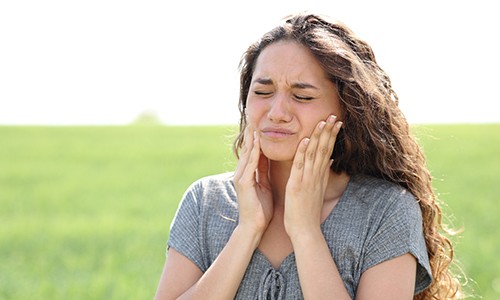 Woman standing outdoors, experiencing symptoms of TMJ disorder